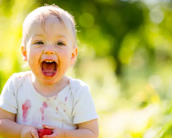 Uśmiechnięte 1.5 roczne dziecko nie mówi mama, ale z radością trzyma truskawkę.