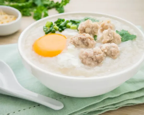 Miseczka pysznego congee z mięsnymi klopsikami, jajkiem i szczypiorkiem. Idealne na rozgrzewający posiłek.