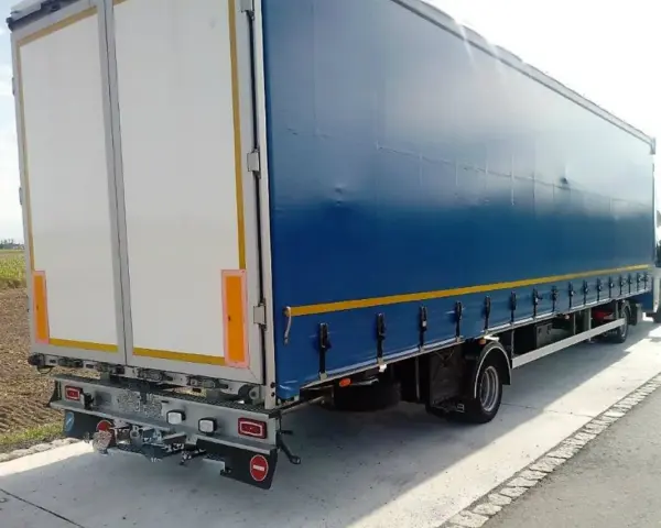 Tylna część niebieskiej naczepy z białymi drzwiami, stojąca na poboczu. To część zespołu pojazdów gotowego do drogi.