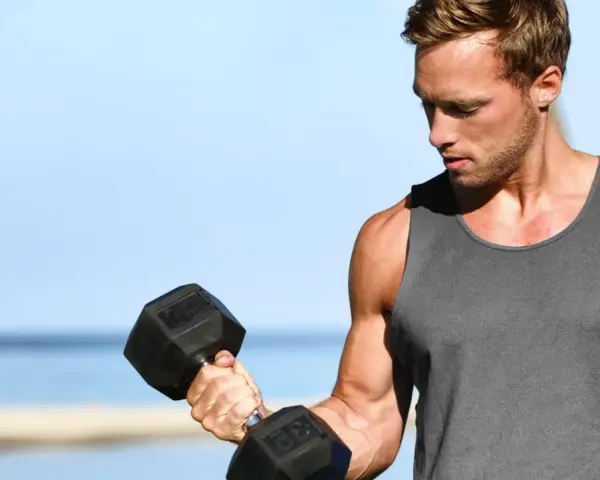 Mężczyzna ćwiczy biceps na plaży, zastanawiając się, ile serii na biceps w tygodniu da najlepsze efekty.