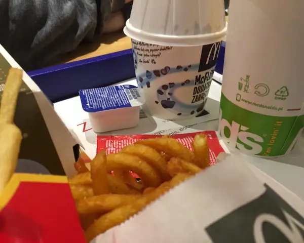 Zakręcone frytki McDonald's w pudełku z sosem i napojem.