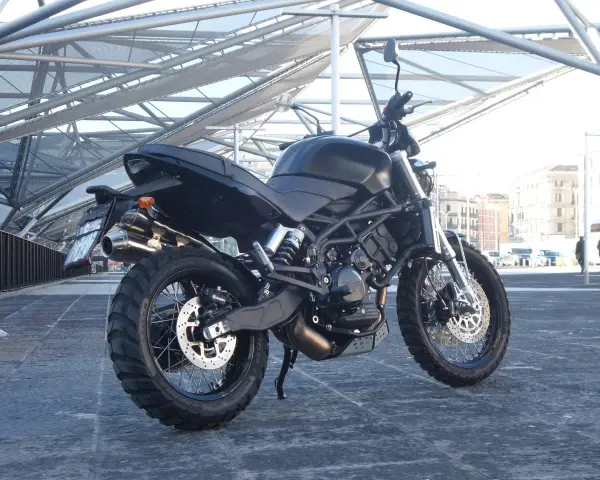 La Moto Morini Scrambler 1200, nera e imponente, si staglia sotto una struttura metallica moderna.