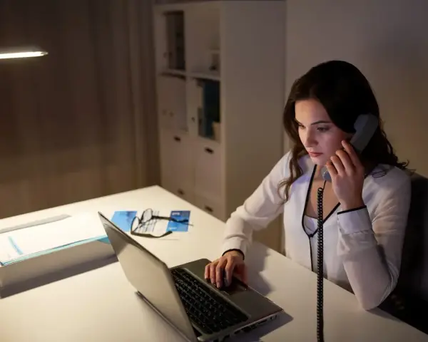Młoda kobieta, dyspozytor, pracuje po godzinach przy laptopie i telefonie.
