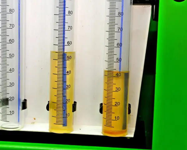 Trzy menzurki z podziałką. W dwóch z nich widać żółty płyn, prawdopodobnie benzyna w oleju, na poziomie około 50 i 40 ml.