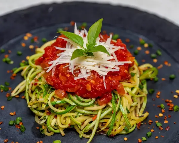 Deliciosa pasta con verduras, hecha de calabacín en espiral, cubierta con salsa de tomate y queso rallado.