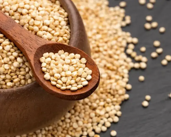 Une cuillère en bois remplie de quinoa cru, posée sur un bol débordant de ces graines nutritives.
