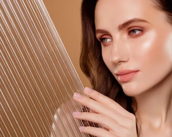 Kobieta z idealną cerą, która emanuje blaskiem, niczym efekt glass skin. Delikatne linie na pierwszym planie dodają głębi.