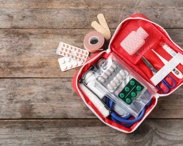 Trousse de secours pharmacie liste : pansements, rouleau de sparadrap, pilules, thermomètre, ciseaux, stéthoscope et masque.