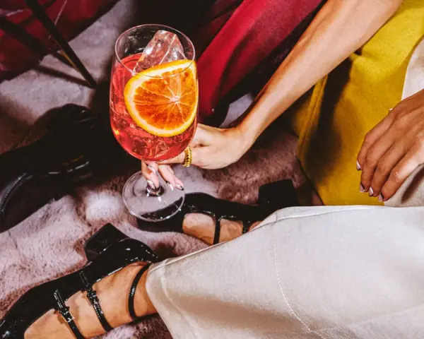 Elegancka kobieta z drinkiem, zastanawia się: martini co to? Złota biżuteria i czarne buty dodają szyku.