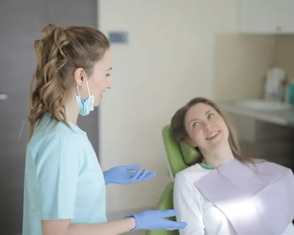 Uśmiechnięta pacjentka na fotelu stomatologicznym słucha dentystki. To obrazek z gabinetu, gdzie odbywają się studia stomatologiczne.