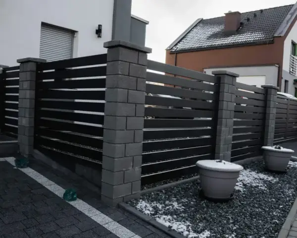 Nowoczesne ogrodzenie z betonowych słupków i ciemnych paneli. Taka wysokość ogrodzenia bez pozwolenia zapewnia prywatność.