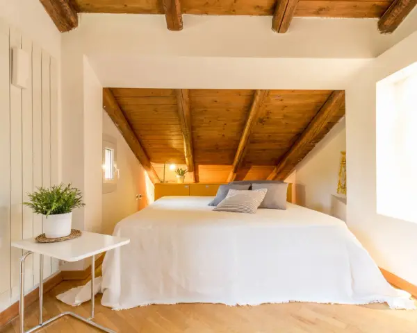 Accogliente camera da letto in mansarda con travi a vista in legno. Idee per un nido romantico e funzionale.