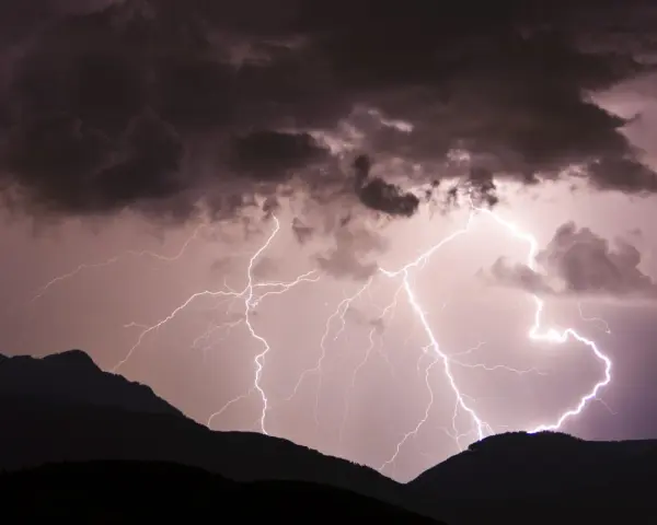 Gewitter in den Bergen: Blitze zucken durch dunkle Wolken über silhouettierten Gipfeln. Ein dramatisches Naturschauspiel.