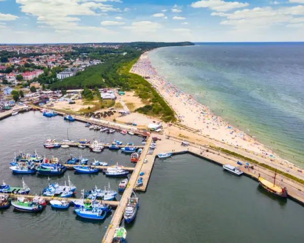 Port rybacki we Władysławowie, województwo pomorskie, tętni życiem. W tle rozciąga się plaża pełna turystów i morze.
