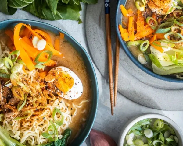 Zwei Schüsseln dampfendes Miso Ramen mit Nudeln, Ei, Karotten, Pak Choi und Frühlingszwiebeln.