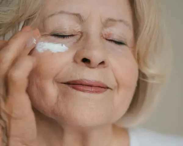 Eine Frau über 70 trägt eine feuchtigkeitsspendende Creme auf. Ihre Augen sind geschlossen, während sie sich um ihre Haut kümmert.