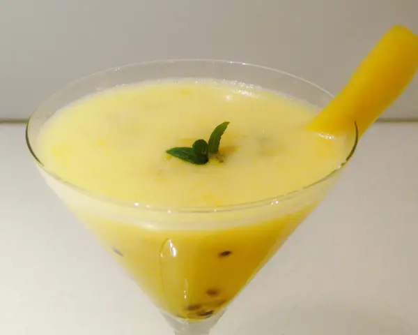Orzeźwiający drink z marakują, ozdobiony listkiem mięty i kawałkiem mango.