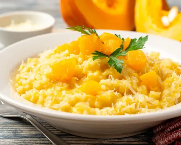 Un cremoso risotto de calabaza, adornado con trozos de calabaza y perejil fresco, espolvoreado con queso rallado.