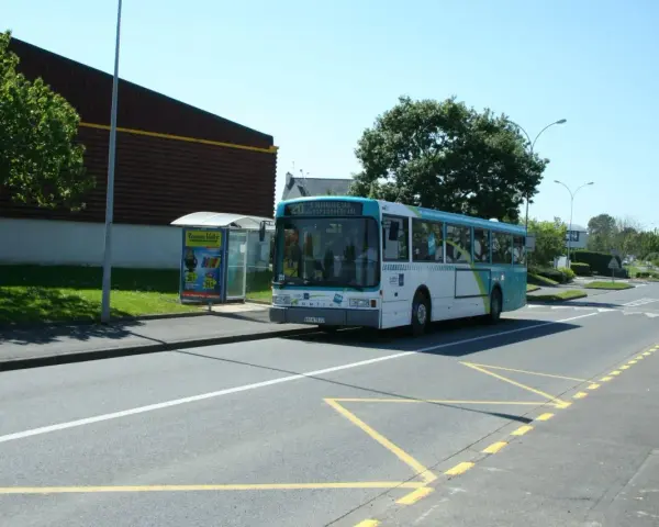 Un bus scolaire s'arrête à un arrêt de bus, respectant le code de la route. Le soleil brille sur la route.