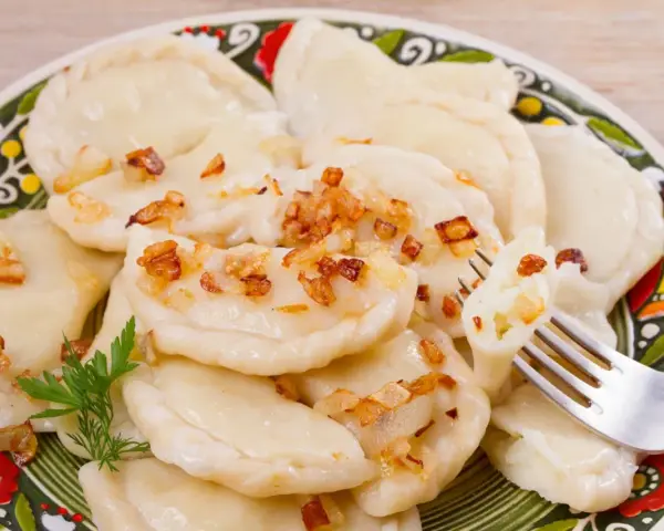 Pyszne pierogi ruskie z farszem Magdy Gessler, posypane skwarkami. Na talerzu z tradycyjnym wzorem.
