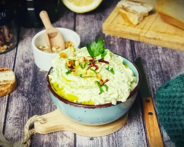 Cremiger Zucchini-Dip mit Pinienkernen und Kräutern, serviert mit geröstetem Brot.