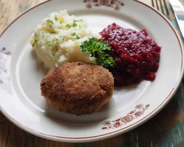 Kotlet mielony z ziemniakami i żurawiną, udekorowany natką pietruszki.