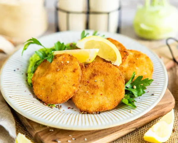 Knusprige Kohlrabi-Schnitzel auf einem Teller mit Erbsenpüree, Zitrone und Petersilie. Ein köstliches vegetarisches Gericht.