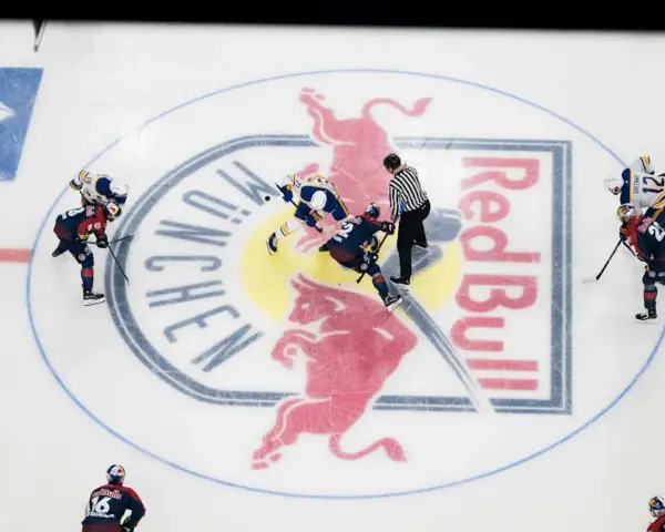 Hokeiści walczą o krążek na lodowisku z logo Red Bull. W hokeju są trzy tercje, a zawodnicy szykują się do kolejnej.