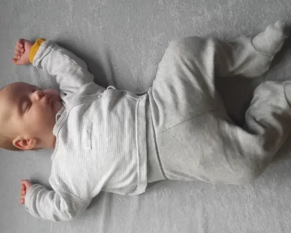 Śpiące dziecko, roczne, leży na plecach. Widać delikatną asymetrię ułożenia rączek i nóżek, co jest naturalne w tym wieku.