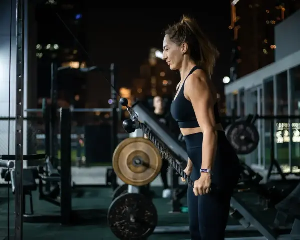 Kobieta ćwiczy na siłowni, korzystając z wyciągu. Jej karta multisport pozwala na takie wieczorne treningi.