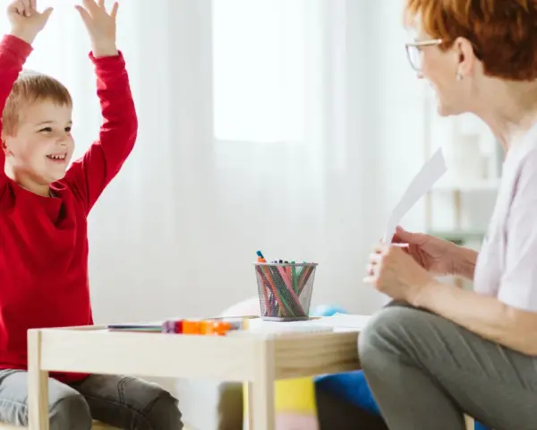 Chłopiec z podniesionymi rękami, uśmiechnięty, podczas sesji terapeutycznej. Może to być pomocne w ocenie objawów ADHD u dzieci test.