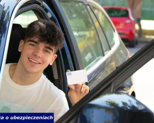 Uśmiechnięty młody kierowca pokazuje prawo jazdy. Cieszy się z nowo zdobytej niezależności i wiedzy o ubezpieczeniach.