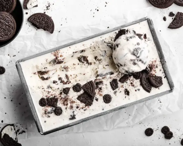 Cremiges Oreo Eis in einer Metallform, garniert mit ganzen und zerbrochenen Keksen. Ein Löffel Eis liegt obenauf.