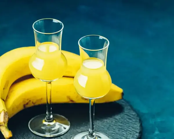 Dwa kieliszki z żółtym likierem bananowym obok dojrzałych bananów. Idealny przepis na domowy likier bananowy.
