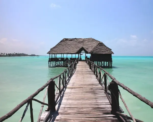 Drewniany pomost prowadzi do chatki na palach na turkusowej wodzie. Idealne miejsce na wiza zanzibar.
