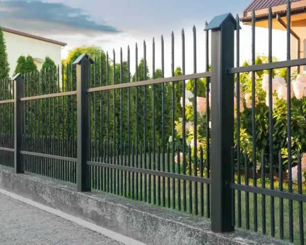 Betonowy murek jako alternatywa dla podmurówki pod ogrodzenie. Czarny metalowy płot z ostrymi zakończeniami.