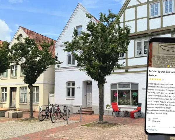 Blick auf die mittelalterliche Itzehoe Altstadt mit Fachwerkhäusern und einem Smartphone, das Informationen über die Stadt anzeigt.