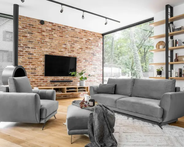 Nowoczesne, szare komplety wypoczynkowe z funkcją spania Black Red White. Wygodna sofa i fotel przy ceglanej ścianie.