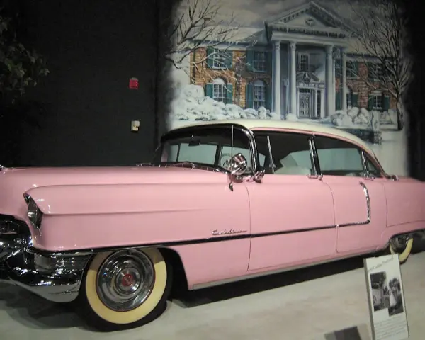 Ein rosafarbener Cadillac, der einst Elvis Presley gehörte, steht vor einer gemalten Kulisse von Graceland.