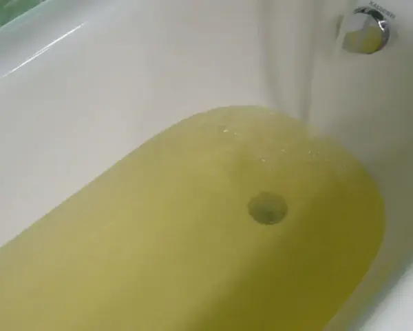 Wanna z żółtą wodą, z kranu leje się woda.