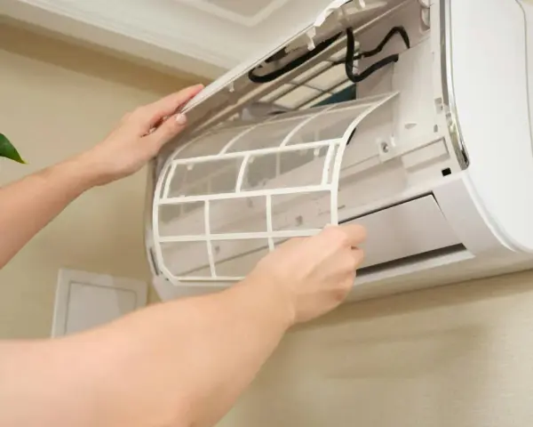 Osoba wyjmuje filtr z jednostki wewnętrznej klimatyzacji split, aby go wyczyścić.