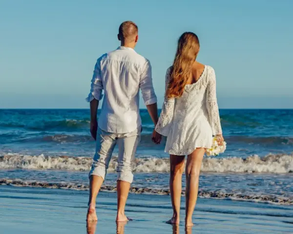Para idąca plażą, trzymająca się za ręce. Ich miłość grecka kwitnie na tle błękitnego morza i nieba.