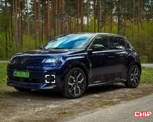 Ciemnoniebieski Renault 5 E-Tech elektryczny stoi na drodze leśnej.