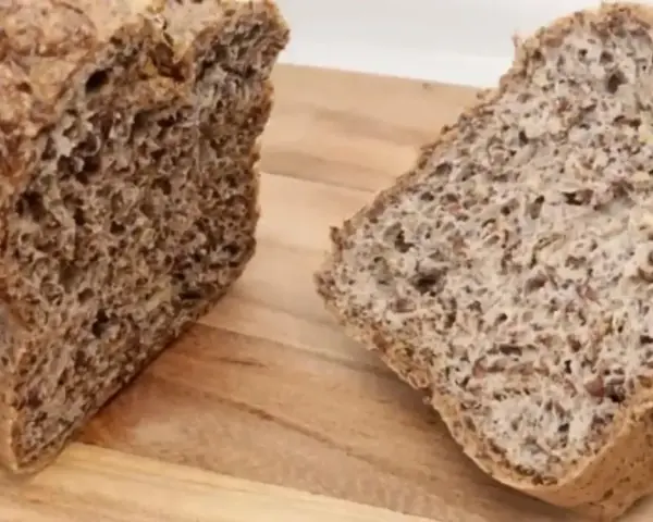 Chleb z siemienia lnianego, pokrojony na desce. Widoczny bochenek i dwa kromki, pełne ziaren.