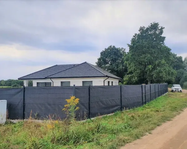 Ciemnoszara siatka na ogrodzeniu panelowym, idealna jako czym zasłonić ogrodzenie panelowe. Dom i samochód w tle.
