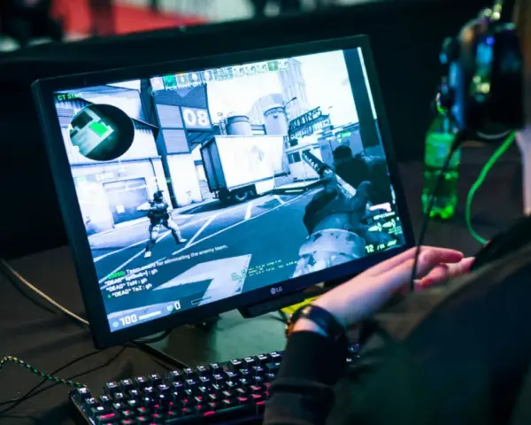 Gracz w słuchawkach gra w CS:GO, próbując jak zmniejszyć ping. Na ekranie widać akcję z gry i klawiaturę.