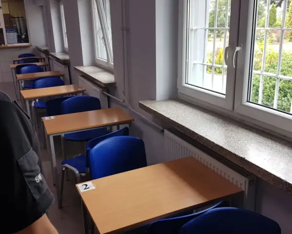 Rzędy pustych ławek i krzeseł w sali lekcyjnej. Za kratami okien widać zieleń. To może być sala egzaminacyjna w więzieniu na Białołęce.