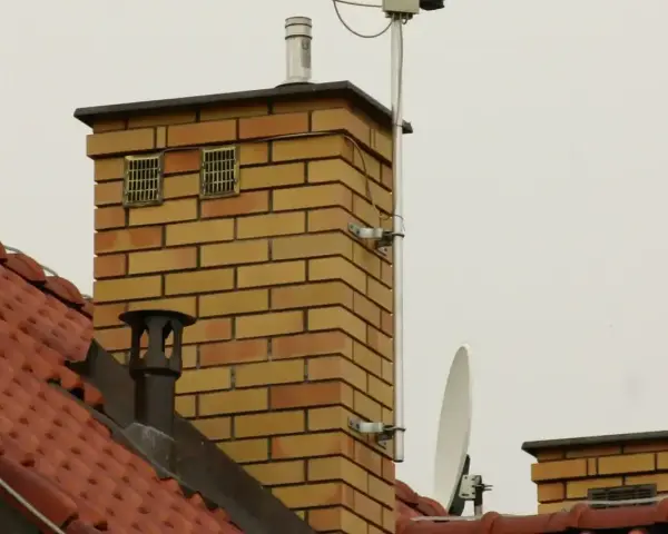 Dwa kratkowane otwory wentylacyjne na ceglanym kominie, zapewniające odpowietrzenie kanału sanitarnego.
