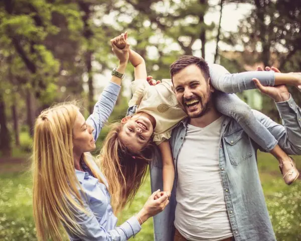 Glückliche Familie im Park. Vater trägt Tochter auf den Schultern, Mutter hält ihre Hände. Kein Anzeichen von Einzelkind-Syndrom, nur pure Freude.
