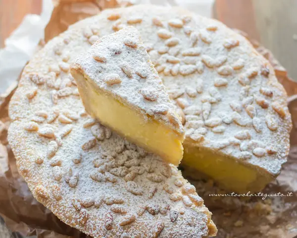 Una fetta di torta della nonna, ricca di crema e cosparsa di pinoli e zucchero a velo, pronta per essere gustata.